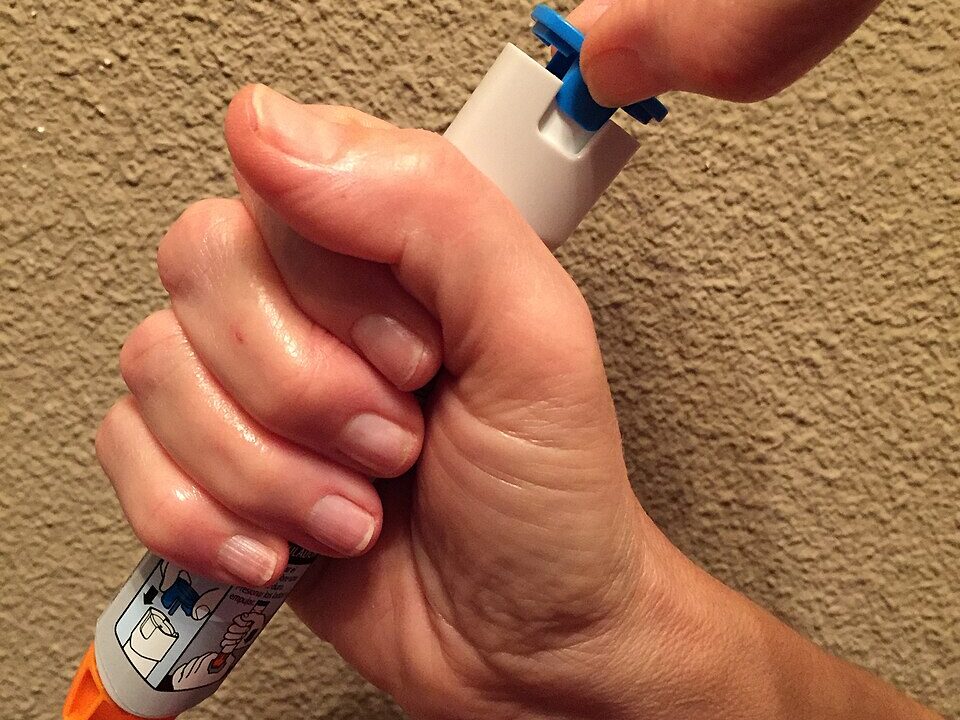 Hand holding an epinephrine autoinjector, the current standard of care for anaphylaxis